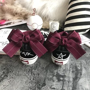 Black canvas casual sneakers featuring oversized maroon ribbon bows on the back heels.