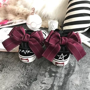 Detail shot of black high-top canvas sneakers featuring oversized burgundy bows on the heel.