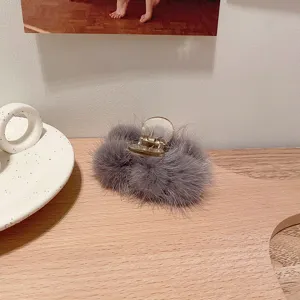 Détail de pince à cheveux en fourrure de vison peluche grise, accessoire élégant sur plateau bois.