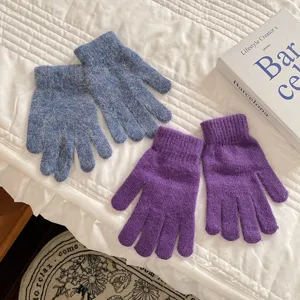 Knit winter gloves detail view, soft plush texture in blue and purple colors on bed.