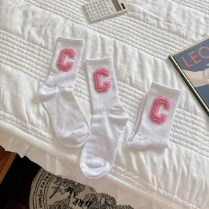 Vue détaillée de chaussettes slouch en coton blanc avec broderies de lettres C roses texturisées.
