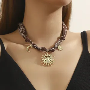 Detailed shot of brown printed fabric scarf choker necklace with gold sun and moon charms.