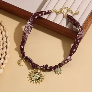 Detail shot of a brown paisley bandana choker necklace featuring gold sun and moon charms.