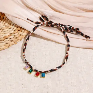 Leopard print silk scarf necklace detail showing chic bowknot and colorful gemstone pendants.