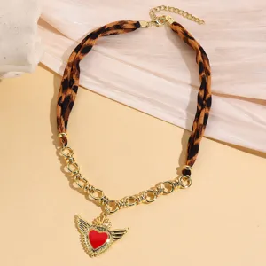 Detail shot of vintage leopard print fabric and gold chain necklace with winged red heart pendant.