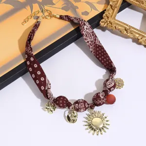 Close-up of retro fabric silk scarf necklace with sun pendant, gold charms, and beaded details.