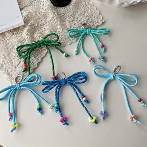 Detailed view of colorful woven bow keychains with beads and charms on lace background.