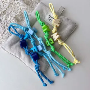 Detail view of handmade braided rope bag charm with colorful letter beads on linen pouch.