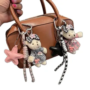 Bolso marrón con bonitos colgantes de peluche de osito a cuadros, lazos y llaveros de estrellas.