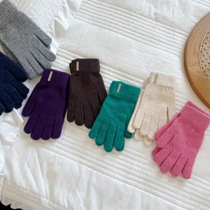 Detail view of colorful winter knitted gloves with metal badge on white background.