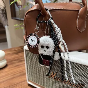 Fluffy curly puppy plush bag charm keychain with poker chip pendant and woven strap detail.