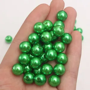 Close-up detail showing dark green ABS plastic imitation pearl beads held in hand for DIY crafts.