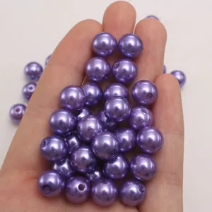 Close-up detail of shiny purple ABS imitation pearl loose beads held in hand for crafts.