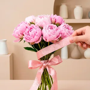 Detailed close-up view of pink satin ribbon bow and peony bouquet crafting accessory, glossy texture.