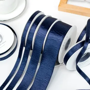 Dark blue satin ribbon roll close-up, shiny velvet fabric material for DIY bows and garment accessories.