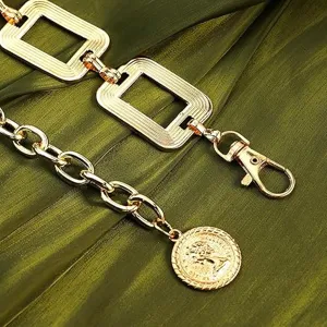 Dettaglio cintura a catena in metallo dorato, maglie geometriche e ciondolo a moneta retro.