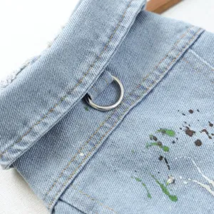 Detail view of the pet denim jacket showing lapel collar, metal D-ring, and colorful paint splatters.