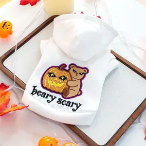 Détail de sweat à capuche pour animal avec broderie ours et citrouille sur tissu blanc doux.