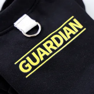 Detalle de primer plano de sudadera negra para mascotas con anilla en D y texto Guardian.