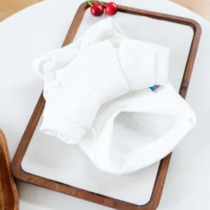 White pet sweatshirt detail view, folded neatly on a wooden tray with cherry decor.