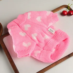 Cute pink pet sweater detail with white heart knit pattern on clean tabletop flat lay.