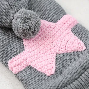 Grey pet knitted sweater closeup, pink star and cute pompom detail, soft warm fabric.