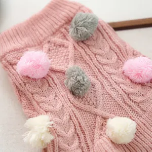 Close-up detail of cute pink knitted pet sweater featuring colorful pom-poms soft warm dog wear