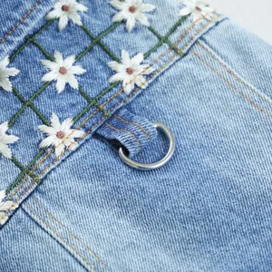 Close-up detail of pet denim apparel featuring cute white daisy embroidery and a metal D-ring.