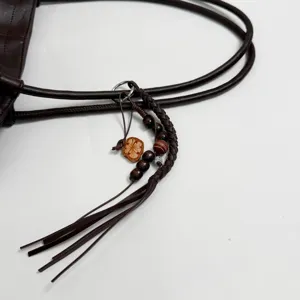 Detail shot of dark brown leather tote bag handle and braided charm pendant decoration.