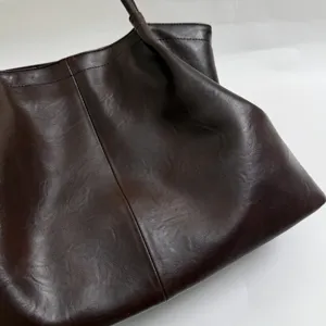 Dark brown oil-wax leather tote bag close-up, premium texture and pleated design details.