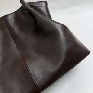 Close-up view of the dark brown oil-wax leather tote bag showing fine texture and pleated design.