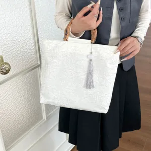 Detailansicht der eleganten weißen Leinentasche mit Bambusgriff und feiner Quaste.