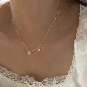 Gros plan d'un collier argenté cœur et étoile avec des zircons noirs porté sur la clavicule.