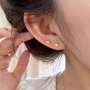 Gros plan détaillé de petites boucles d'oreilles puces cœur en or portées, design fin.