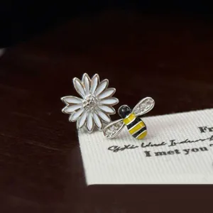 Détail en gros plan des boucles d'oreilles asymétriques en argent marguerite et abeille.