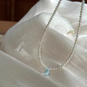 Gros plan délicat de collier de perles avec pendentif gemme bleu clair en forme de goutte.