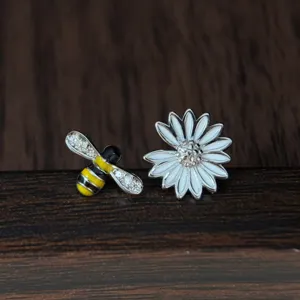Gros plan détaillé de boucles d'oreilles asymétriques abeille marguerite en argent.