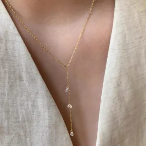 Gros plan détaillé d'un collier Y doré minimaliste et délicat orné de minuscules cristaux.