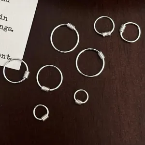 Détail de petites créoles argentées montrant des ressorts pour piercing minimaliste.
