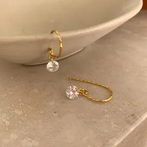 Gros plan de boucles d'oreilles pendantes minimalistes en argent doré avec cristal étincelant.