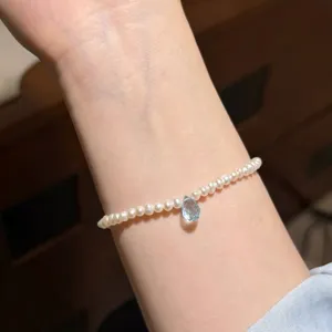 Gros plan détaillé d'un délicat bracelet de perles blanches avec un pendentif goutte bleu clair.