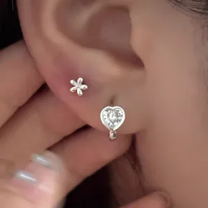 Gros plan détaillé de boucles d'oreilles cœur en zircon et fleurs en argent portées, empilables.