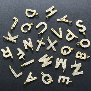 Primo piano dettaglio di ciondoli lettere alfabeto in rame placcato oro con zirconi.