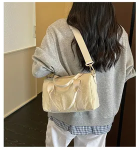 Gedetailleerd overzicht van een veelzijdige beige cilindrische schoudertas gedragen.