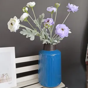 Close-up detail of artificial ranunculus flower arrangement in blue ceramic vase for home decor.