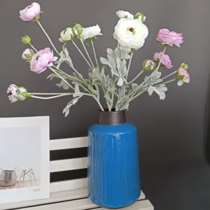 Detailed close-up of artificial ranunculus flowers in blue ceramic vase with home decor prop.