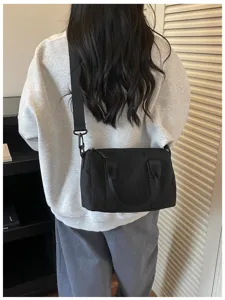 Detail view of a solid black canvas crossbody bag worn on shoulder, casual commuter style.