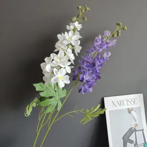 Vista dettagliata di un ramo di delphinium artificiale con petali realistici e foglie verdi.
