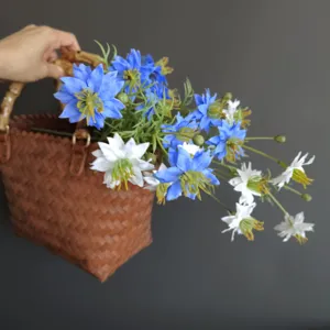 Detail shot of artificial blue and white wildflowers in a woven basket with bamboo handle.