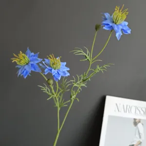Close-up of artificial blue nigella flower branch, delicate petals and fine green leaves decor.